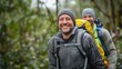 © Karat - A smiling middle-aged man hiking in a forest, wearing a grey jacket and beanie, carrying a yellow backpack, with another hiker visible in the background, symbolizing outdoor adventure and camaraderie.