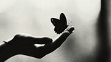   A B&W photo of a person handing a butterfly in its palm, with a window in the background