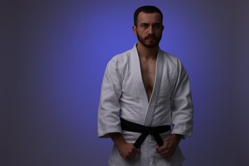 Wall Mural - Karate fighter in uniform on dark purple background. Space for text