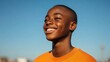 © Lion - Teenage boy with dark skin, buzz cut, and a wide smile, playing basketball on an outdoor court, urban setting with bright sunlight and clear blue sky