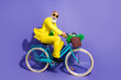 © deagreez - Photo of cheerful glad optimistic senior man dressed yellow trendy clothes riding bicycle isolated on purple color background