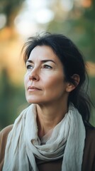 Wall Mural - Middle aged woman with dark hair, wearing casual clothing, looking thoughtfully into the distance, blurred natural background, soft natural light, minimalistic style