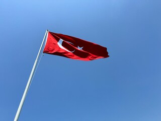 Turkish Flag. Turkish flag flutters in the wind on a flagpole against a blue sky background. Turkish flag photo for Turkish national day celebration.