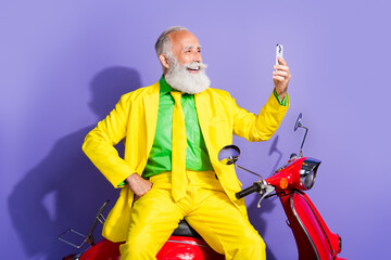 Wall Mural - Photo of extravagant positive funny pensioner wearing yellow trendy costume using phone isolated on purple color background