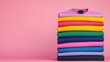 © Nitchalee N. - Display of colorful t-shirts concept, A stack of colorful folded sweaters against a pink background, showcasing a vibrant array of hues and textures.