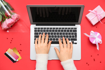 Wall Mural - Female hands with modern laptop, credit cards, flowers and gifts for Valentine's Day on red background, closeup