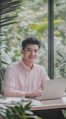 Poster - Young man working on laptop in a bright, minimalist indoor space surrounded by lush greenery