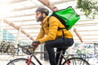 © oneinchpunch - Food delivery rider on his bicycle. Image of a middle age man at work in the city center. Delivering pizza and burgers at home with the thermal backpack
