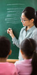 © Aleksandra - Asian Female Teacher Writing on Chalkboard in Classroom with Young Students Observing