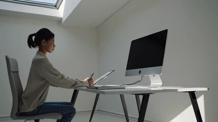 Poster - Young woman working diligently at her desk in a bright, modern workspace with a computer and tablet