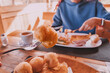 © EdNurg - Fork holding a traditional rural Montenegro priganice fried donut at a restaurant with a woman having breakfast in the background