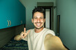 © Davide Angelini - Happy handsome guy taking selfie with smartphone at home - Laughing guy looking at camera - People and technology concept