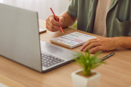 Cropped photo of businessman writing tasks and to do list in his notepad sitting at the desk with laptop at home or at office. Man looking to schedule calendar planning daily appointment.
