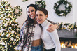 © BullRun - Happy sisters hugging for photograph in room decorated for Christmas