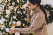 © BullRun - Cheerful young woman decorating Christmas tree and talking on smartphone