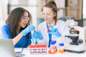 Two beautiful female doctors sitting at a table in a science lab with test flasks. Colorful glass bottles filled with various liquids on table with microscope