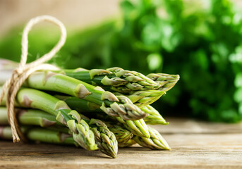 Fresh bunch of asparagus tied with twine resting on a rustic wooden table with parsley in the background