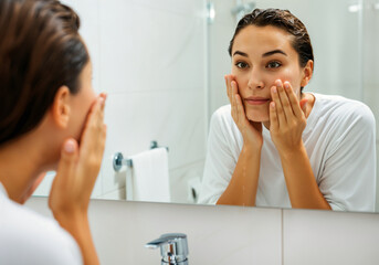 Wall Mural - Woman gently cleansing her face with water in the bathroom, focusing on skincare routine