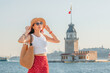 © EdNurg - A woman traveler in a stylish hat poses near Kiz Kulesi (Maiden's Tower), capturing the scenic beauty of the Bosphorus waterfront in Istanbul
