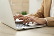 © New Africa - Businesswoman using laptop at wooden table indoors, closeup. Modern technology