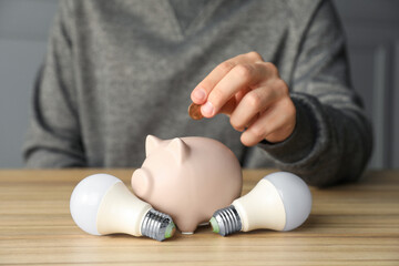 Wall Mural - Man putting coin into piggy bank at wooden table, closeup. Energy saving concept