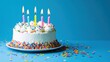 © red_orange_stock - A festive birthday cake adorned with colorful sprinkles and lit candles sits on a bright blue background, perfect for celebrations