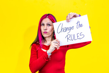 Woman showing sign reading change the rules on yellow background