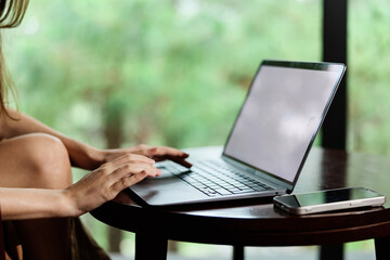 Canvas Print - Young woman working on a laptop at home, creating a relaxed atmosphere with greenery in the background, conveying productivity and modern lifestyle