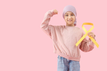 Little girl after chemotherapy with yellow ribbon showing muscles on pink background. Childhood cancer awareness concept