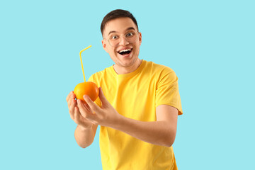 Young man holding orange with straw on blue background