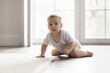© fizkes - Tireless explorer. Portrait of happy active adorable little infant baby feel healthy in comfy diaper white sleeveless suit of natural cotton crawl play alone on warm floor with heating in family house