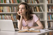 © fizkes - Learning is hard. Pensive adolescent female young scientist undergraduate student sit at library desk by notebook screen hold pen look aside ponder on research topic create ideas for diploma project