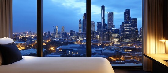 Poster - Cozy bedroom view revealing a panoramic city skyline with urban architecture and vibrant nightlife illuminated at dusk.