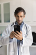© fizkes - Serious middle aged doctor man using mobile phone for Internet communication, giving online consultation to patients, typing on smartphone in clinic office, using medical application, web service
