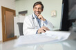 © fizkes - Cheerful middle aged practitioner doctor man working at computer in hospital office, sitting at workplace, looking away with toothy smile, thinking on successful job case, Internet technology
