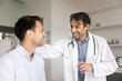 © fizkes - Happy cheerful Latin medical specialist expressing support to positive patient, touching back of man in clinic examination room, sharing good news from test results, medical reports