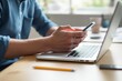 © PlanetOfVectors - Hands holding smartphone near laptop on a wooden desk, natural lighting, blurred background. Concept of multitasking, communication, work. Ai generative