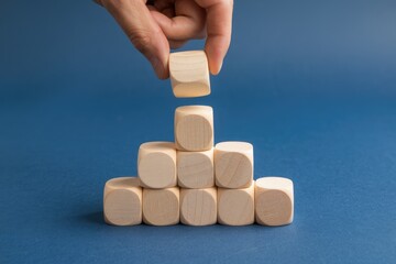 Aufkleber - A hand placing a wooden block on top of a pyramid made of wooden blocks