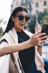 Wall Mural - Happy beautiful asian woman in sunglasses and casual wear using mobile phone for making video call in roaming, cheerful female blogger influencer using smartphone for communication with followers