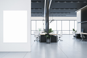 Poster - Modern office interior with blank vertical canvas on white wall and workspace with desks, chairs, and large windows. 3D Rendering