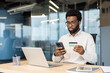 © Liubomir - Man with bank credit card and phone making online payment, serious and focused businessman working inside office with laptop.