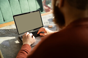 Bearded man sitting using laptop sitting in cafe. laptop white blank screen mockup for display