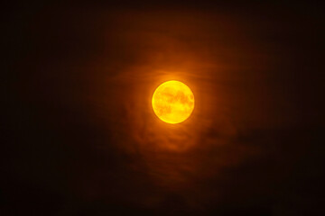 Glowing full moon shining brightly in dark night sky surrounded by soft clouds illuminated with golden light.