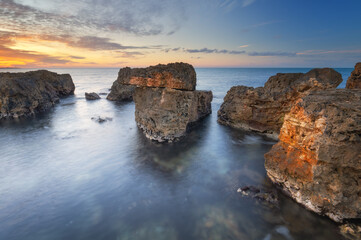 Wall Mural - Beautiful nature seascape of beach shore among rocks on evening sunset.