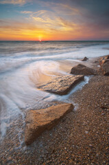 Wall Mural - Stones and sea during the sunset. Beach shore among rocks and stones on evening sunset.