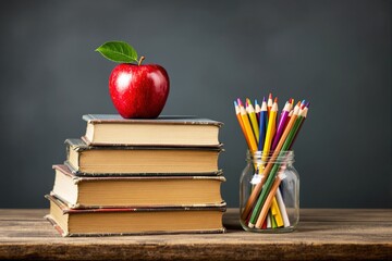 Poster - Apple on books with jar of colored pencils on wooden table, dark background.