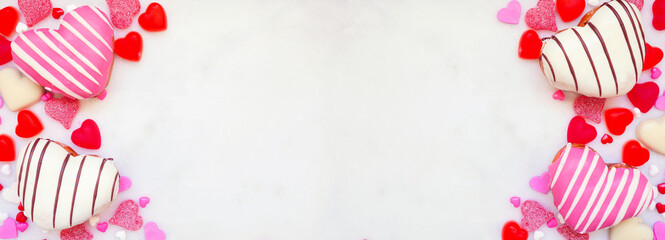 Poster - Valentines Day heart shaped sweets double border with donuts and candies. Top down view on a white marble banner background with copy space.