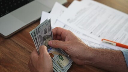 Poster - Meticulously counting stack of dollar banknotes male accountant prepares to fill out collection of tax documents related to office expenses slow motion