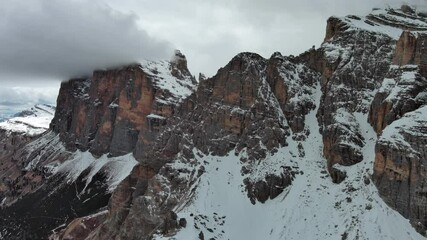 Wall Mural - aerial view of amazing rocky mountains in snow under moody gray clouds, dolomites, italy, 4k
