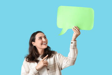 Young woman pointing at blank speech bubble on blue background